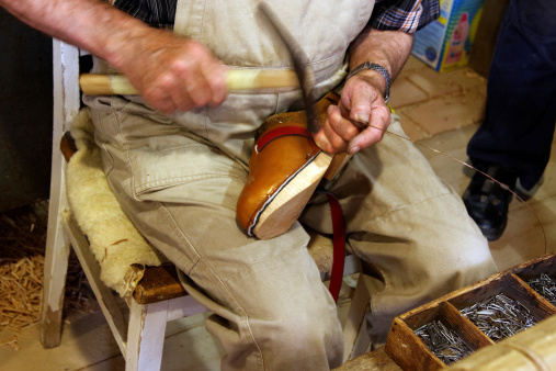 old shoemaker with hammer (blurred motion) nails leather on wooden sole of shoe