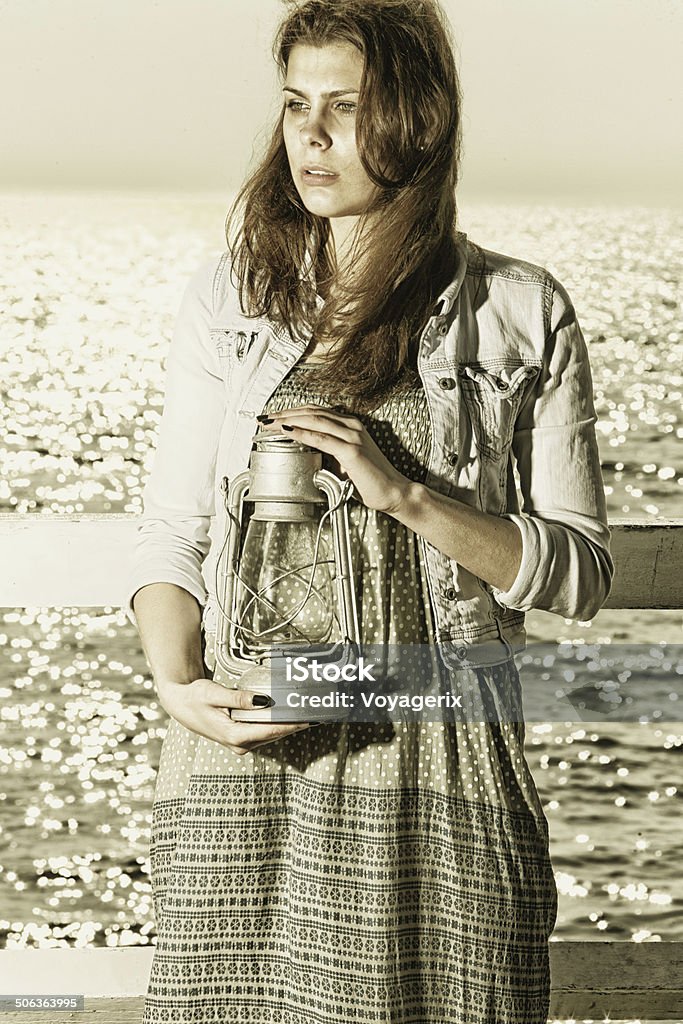 Girl on pier with kerosene lamp Sepia photo. Young woman on pier with a oil kerosene lamp. Concept carrying light, daylight Adult Stock Photo