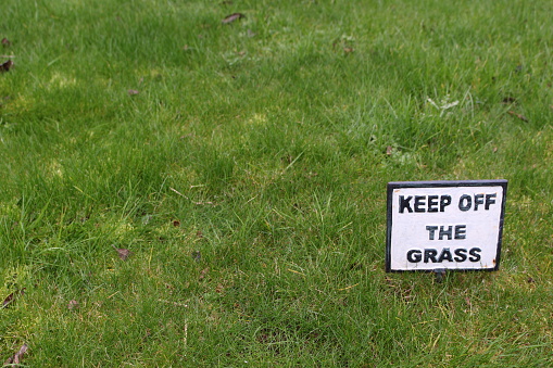 Black and white 'keep off the grass' sign with grass around. Lots of negative space.