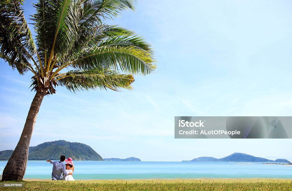 Couple sitting near the sea Happy young caucasian couple sitting under palm near the sea Adult Stock Photo
