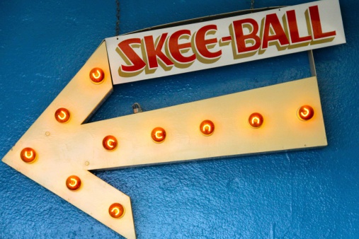 This is a vintage/antique Skee-Ball arrow sign hung on an arcade wall.