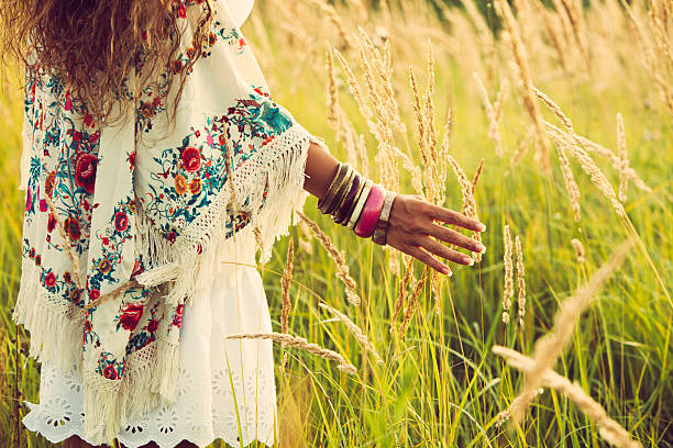 boho fashion woman wearing boho style clothes touching grass, hand with lot of braceletes, summer day in the field, retro colors bohemian fashion stock pictures, royalty-free photos & images