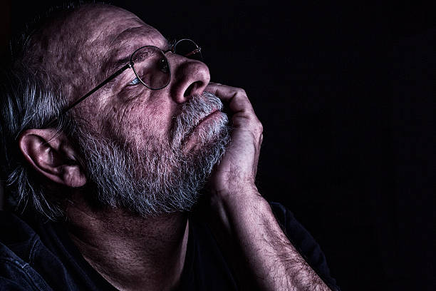 istock Dark Room Senior Man Reading With Chin On Hand 506400330