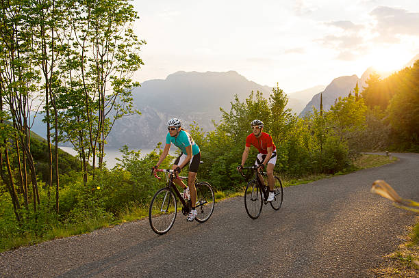 ciclista andare in bicicletta dietro al tramonto - cyclist cycling road women foto e immagini stock