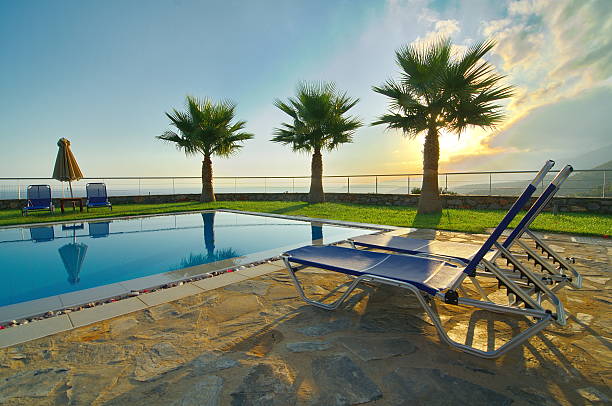 Resting chairs next to pool on hotel roof and next to beach. Sunset over clear water. Mountain in the background. Copy space.