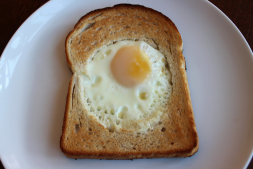 Photo showing a simple breakfast of 'egg in a hole', on a round white plate.  This breakfast is rather like white toast with a circular fried egg in the middle.