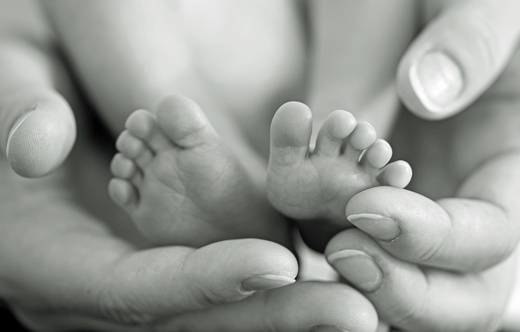 Mother gently hold baby legs in hand. Black and white image with soft focus on babie's feet