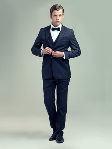 A full length studio portrait of a dapper young man wearing a vintage suit and bow tie