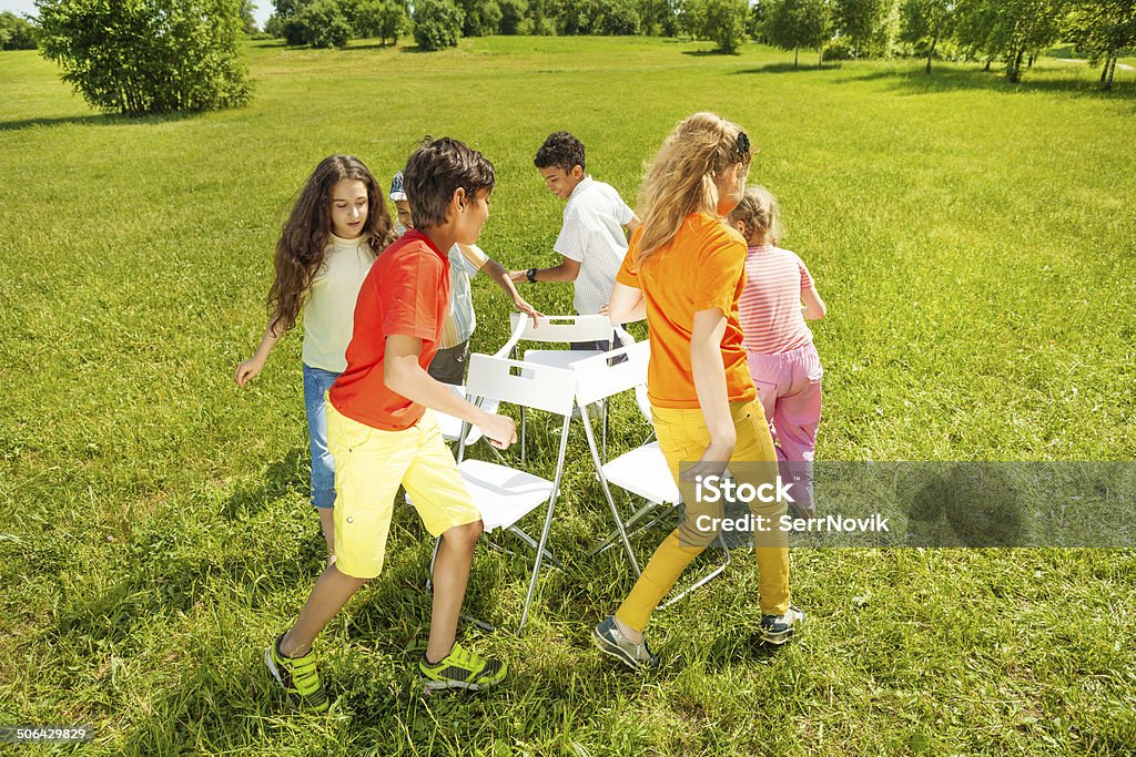 Kids run around playing musical chairs game Kids run around chairs playing a game outside in summer period Musical Chairs Stock Photo