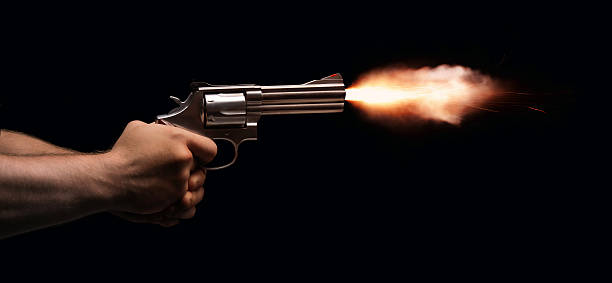 Gun Fire A revolver held by two anonymous hands is fired on a black background. gun revolver stock pictures, royalty-free photos & images