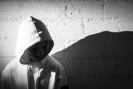 upset teenage boy dressed in hooded jacket leaning against a wall