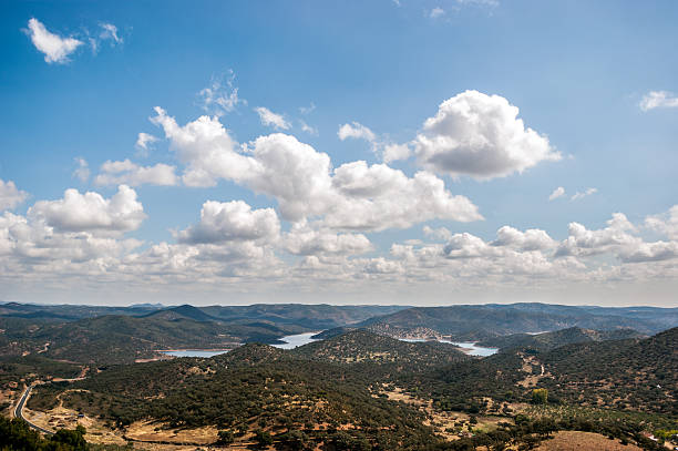 Landscape of mountains with clouds in the sky Landscape of covered mountains with green trees and the blue sky with white clouds, in the nature reserve of Aracena's Saw, Huelva, Spain. Between the mountains there is a lake serrated stock pictures, royalty-free photos & images