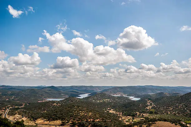 Landscape of covered mountains with green trees and the blue sky with white clouds, in the nature reserve of Aracena's Saw, Huelva, Spain. Between the mountains there is a lake