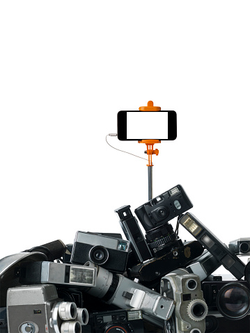 Modern smartphone placed on a selfie stick on top of old fashioned cameras.Large amount of old fashioned cameras are placed on bottom of frame.Isolated on white backgorund with clipping path.Shot with medium format camera Hasselblad in studio.The screen of smartphone is blank white.