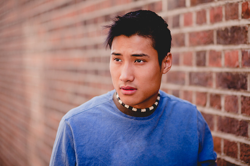 Asian man in plain blue shirt with a brick wall background