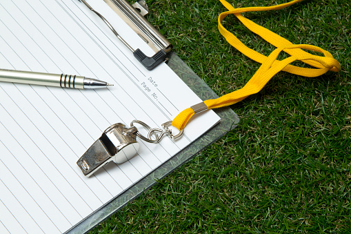 Clipboard with metal sport whistle, pen and paper sheet on grass