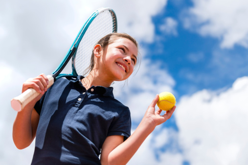 Girl taking tennis lessons and holding racket and ball