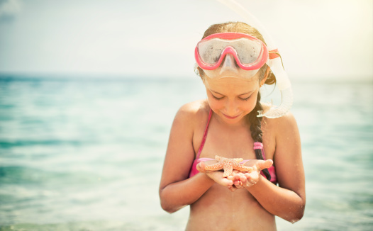 Little girl having fun snorkeling, holding a starfish.