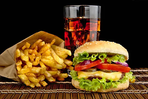 Photo of Cheeseburger, french fries, glass of cola on mat on black