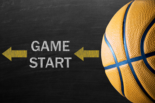 Yellow basketball against blackboard on which GAME START written.