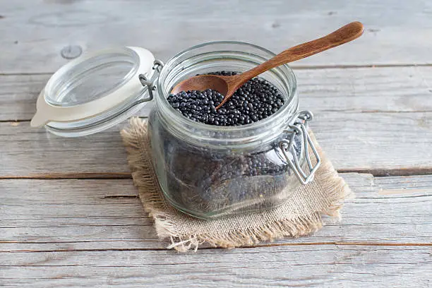 Black Lentils on a glass jar with a spoon on a wooden table
