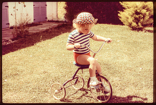 Grainy retro image of a cute girl riding a tricycle. original photographic slide.