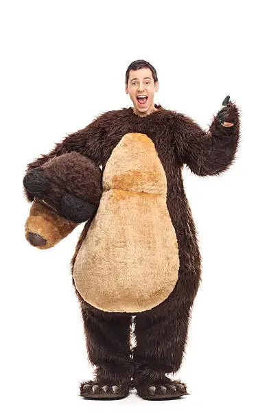 Full length portrait of a young joyful guy in a bear costume giving a thumb up isolated on white background