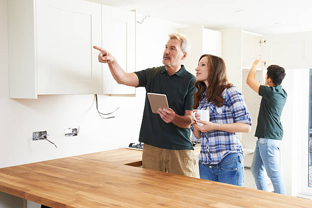 Woman With Carpenter Looking At Plans For Kitchen