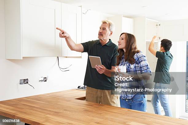 Woman With Carpenter Looking At Plans For Kitchen Stock Photo - Download Image Now - Quality Control, Home Interior, Design Professional