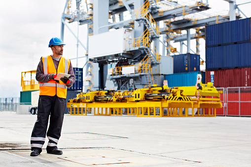 Shot of a young man in workwear using a digital tablet while standing on a large commercial dock