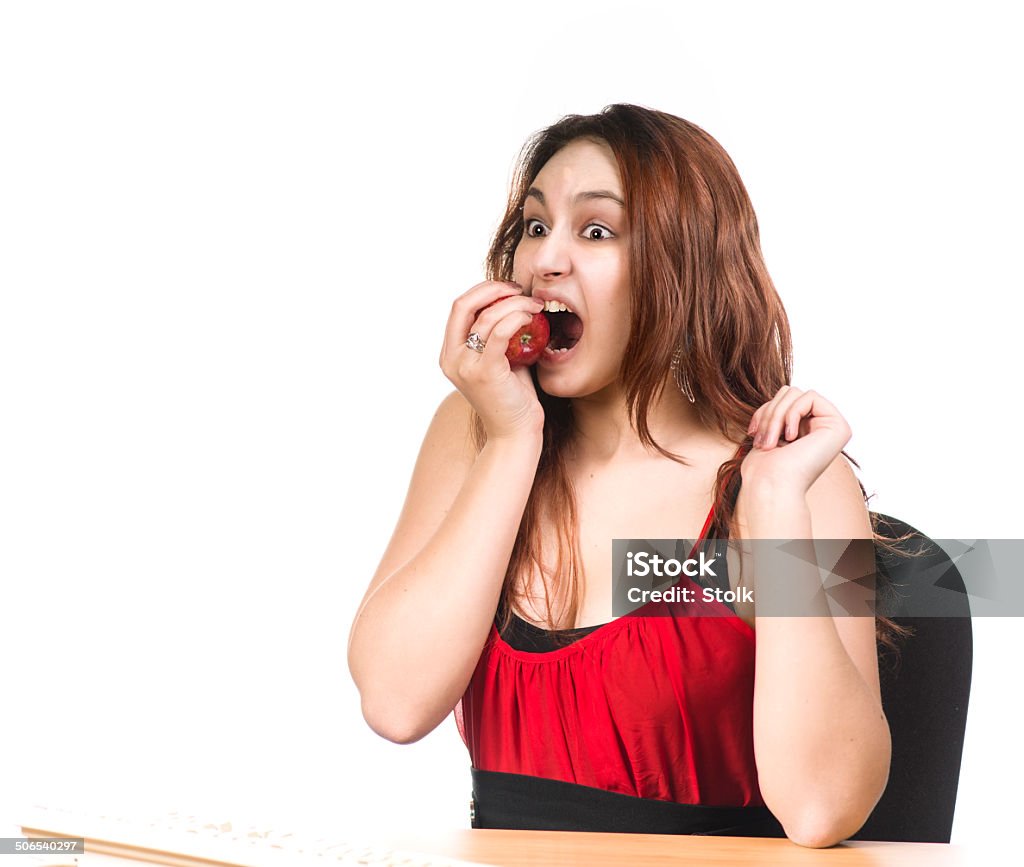 Big bite A Caucasian girl with red hair behind a desk showing an apple against a white background Adult Stock Photo