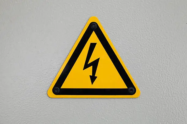 High voltage triangle warning sign mounted on gray metal wall
