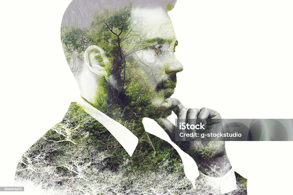 Think green. Digitally composed side view picture of young businessman holding hand on chin and looking away over the picture of green forest Multiple Exposure Stock Photo