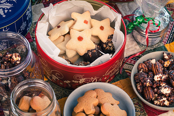 Colorful bird's eye view of various shortbread and gingerbread cookies and chocolate popcorn and cranberry claret wrapped in cellophane all on a patchwork quilted table runner.