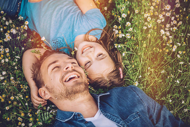 You'll always be my little girl Father and his cute daughter having fun outdoors in a meadow. Lying on green grass and daisy flowers, embracing. Caucasian, blond hair. flower outdoors day loving stock pictures, royalty-free photos & images