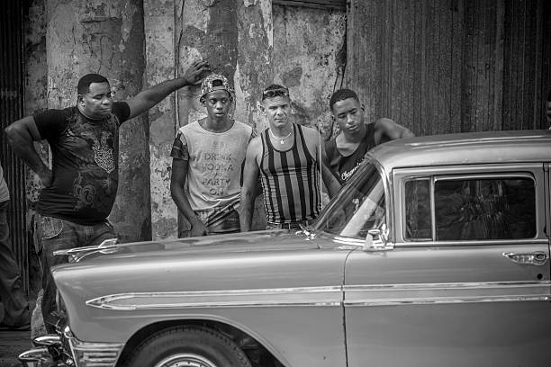 Havana, Cuba - November 10, 2015: busy street corner in Old Havana, near Capitolio. Local Taxi stop with vintage American cars. Group of men hanging out on the street corner, discussing the condition of the parked car.  One of countless vintage US made cars imported to Cuba before the Revolution but still running after more than 50 years due to ingenuity of Cuban car mechanics and some help of various old car parts, including the left over of Russian diesel engines. Large number of these cars are getting restored and used as TAXI cars for up and coming (mostly) US tourists, for the average price of $25US/hour.
