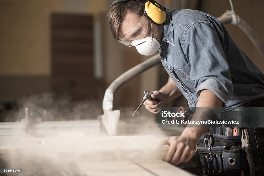 Professionally dressed carpenter varnishing board Horizontal view of professionally dressed carpenter varnishing a board Dust Stock Photo