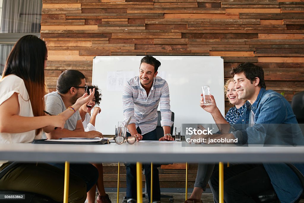 Happy young people having a business meeting Group of happy young people having a business meeting. Creative people sitting at table in boardroom with man explaining business strategy. Travel Agency Stock Photo