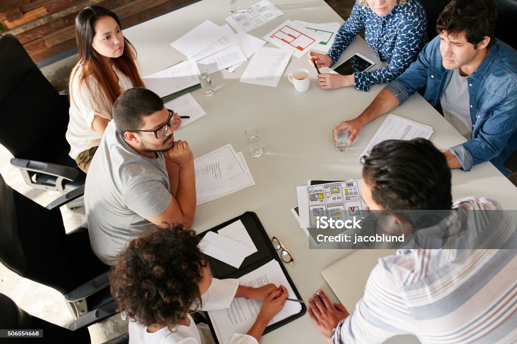 Team of creative professionals meeting in conference room High angle view of creative team sitting around table discussing business ideas. Mixed race team of creative professionals meeting in conference room. Real Estate Office Stock Photo