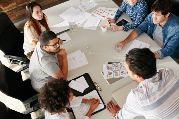 Team of creative professionals meeting in conference room High angle view of creative team sitting around table discussing business ideas. Mixed race team of creative professionals meeting in conference room. real estate office stock pictures, royalty-free photos & images