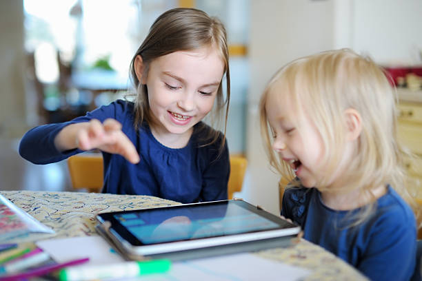 zwei kleine schwestern spielen mit einem digitaltablett - family child portrait little girls stock-fotos und bilder