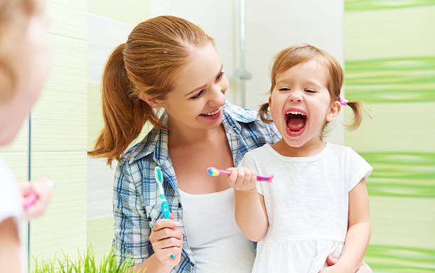 felice famiglia madre e bambino ragazza pulisce i denti con spazzolino da denti - healthy lifestyle human teeth adult brushing foto e immagini stock