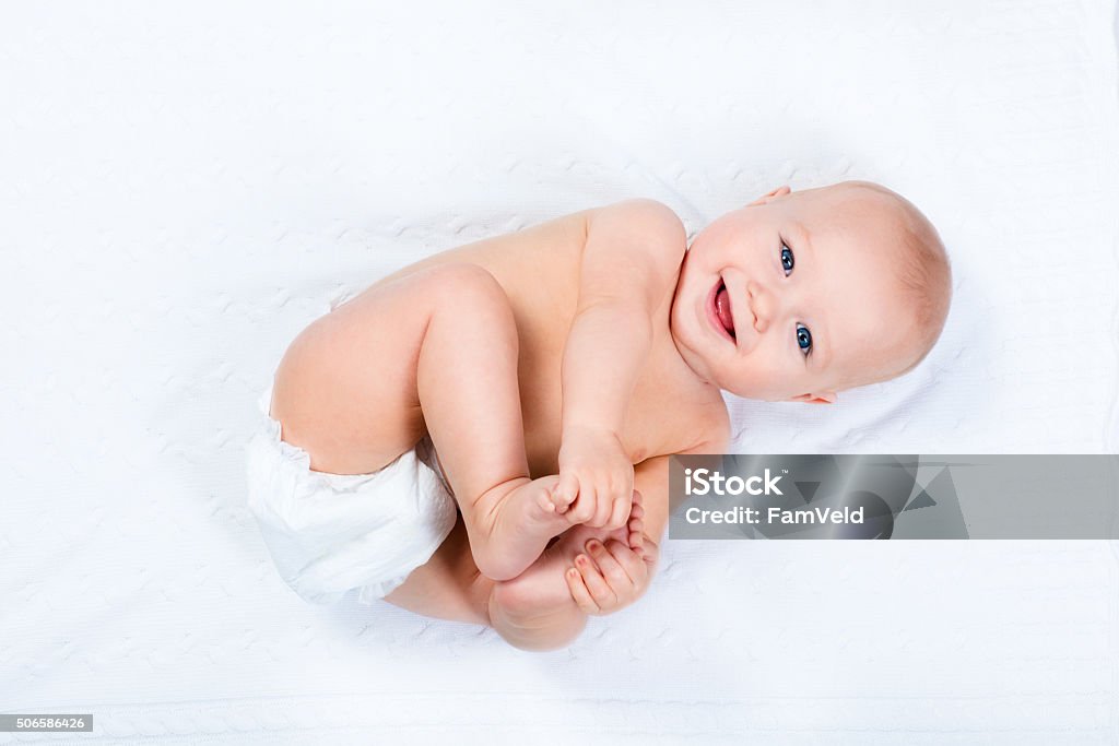 Little baby wearing a diaper Funny little baby wearing a diaper playing on a white knitted blanket in a sunny nursery. Child after bath or shower on a fresh towel. Infant nappy change and skin care. Cute kid playing with his feet Baby - Human Age Stock Photo