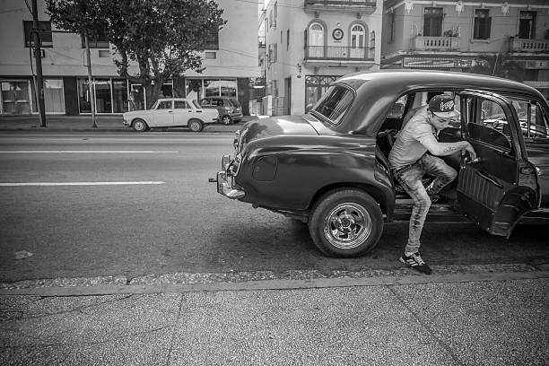 Havana, Cuba - November 10, 2015. Old American made car  parked along Havana Boulevard, Cuba.  Passengers getting outof the car. City street in the background. One of countless vintage US made cars imported to Cuba before the Revolution but still running after more than 50 years due to ingenuity of Cuban car mechanics and some help of various old car parts, including the left over of Russian diesel engines. Most of these cars run across the city as TAXI for local Cubans. Some cars, that are restored completely and looking as new are in use now for foreign tourists only, with hourly rate of $25 per hour.