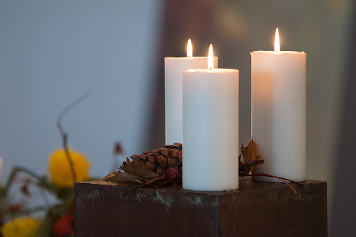 Candle decorated with peaces of Christmas tree, light and ornaments. White Candles and little ceramic houses.