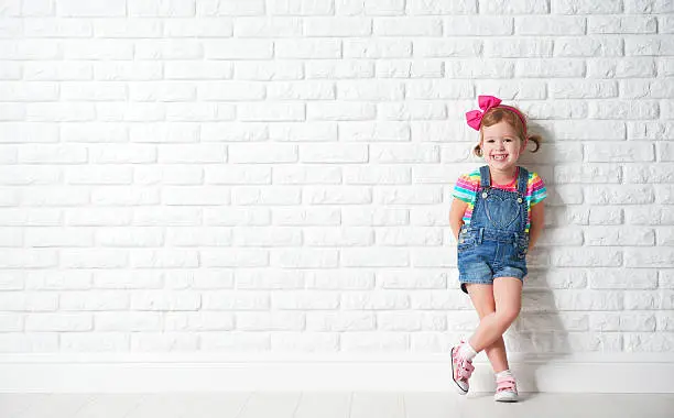 Photo of Happy child little girl laughing at blank brick wall