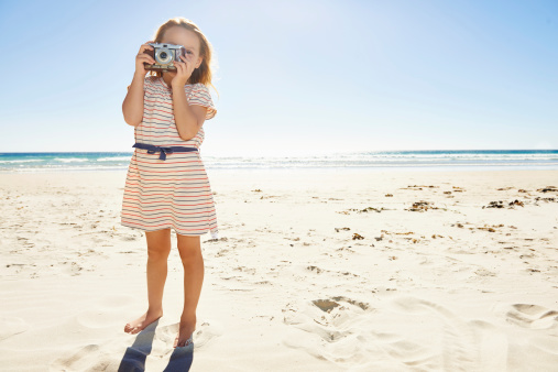 Full length shot of a young girl holding a camera on a beach