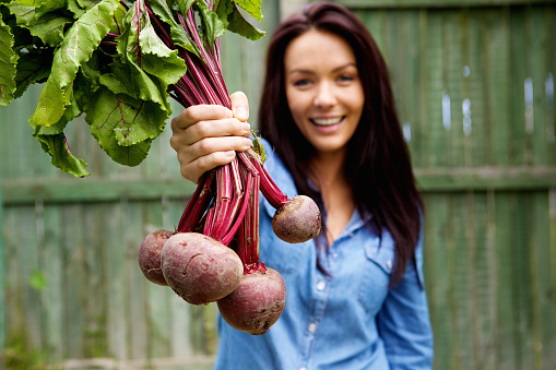 Close up portrait of a smiling woman showing a bunch of beetroots
