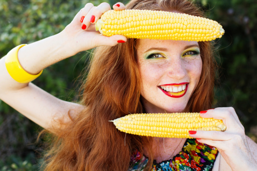 Portrait of a redheared smiling girl holding an appetizing corn cob