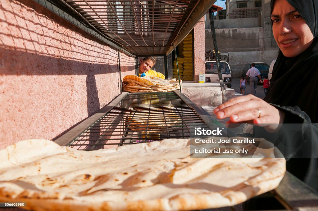 Buying bread in Damascus, Syria Damascus, Syria - June 5, 2010: A Syrian woman gathers her bread from a cooling rack outside a neighborhood bakery while her daughter looks on. The bread is still hot when bought and the customer immediately spreads it out to cool and dry for perhaps two or three minutes before restacking it for the journey home. Syria Stock Photo